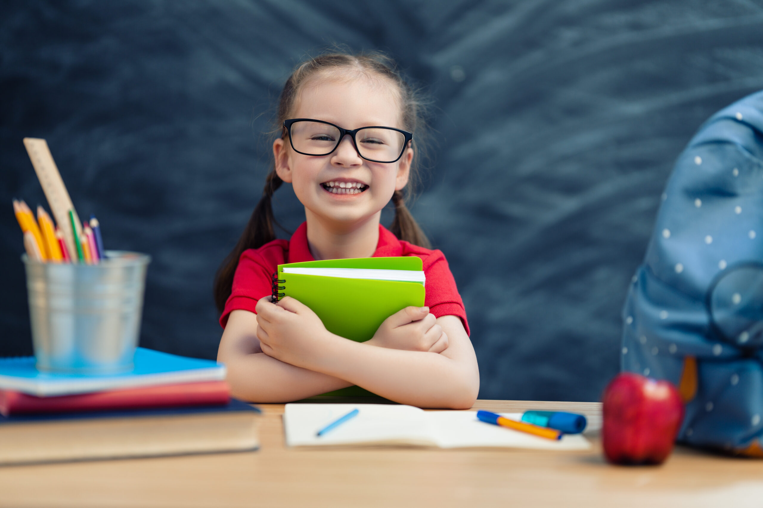 Back to school! Happy cute industrious child is sitting at a desk indoors. Kid is learning in class on background of blackboard.